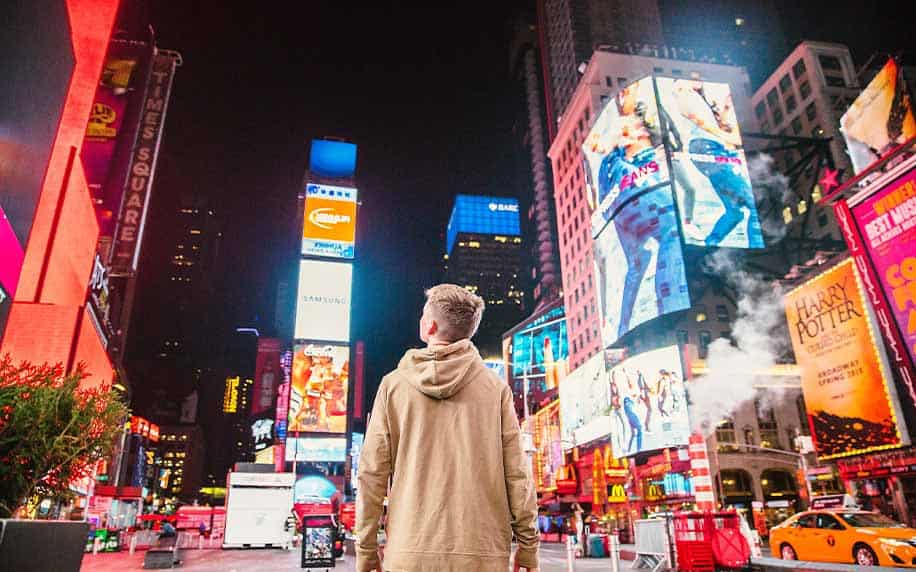 man staring at copy on bright billboards in a city