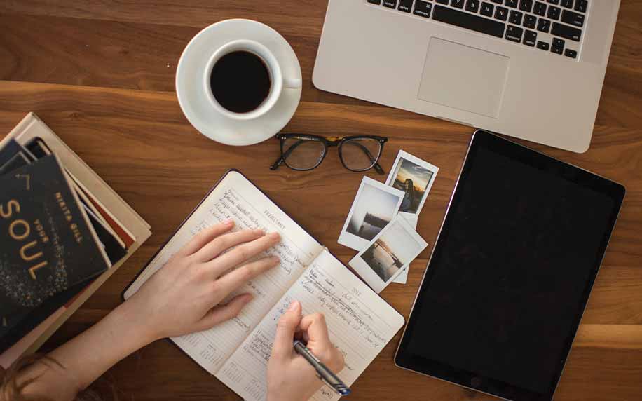 someone researching and writing copy into a book with a coffee