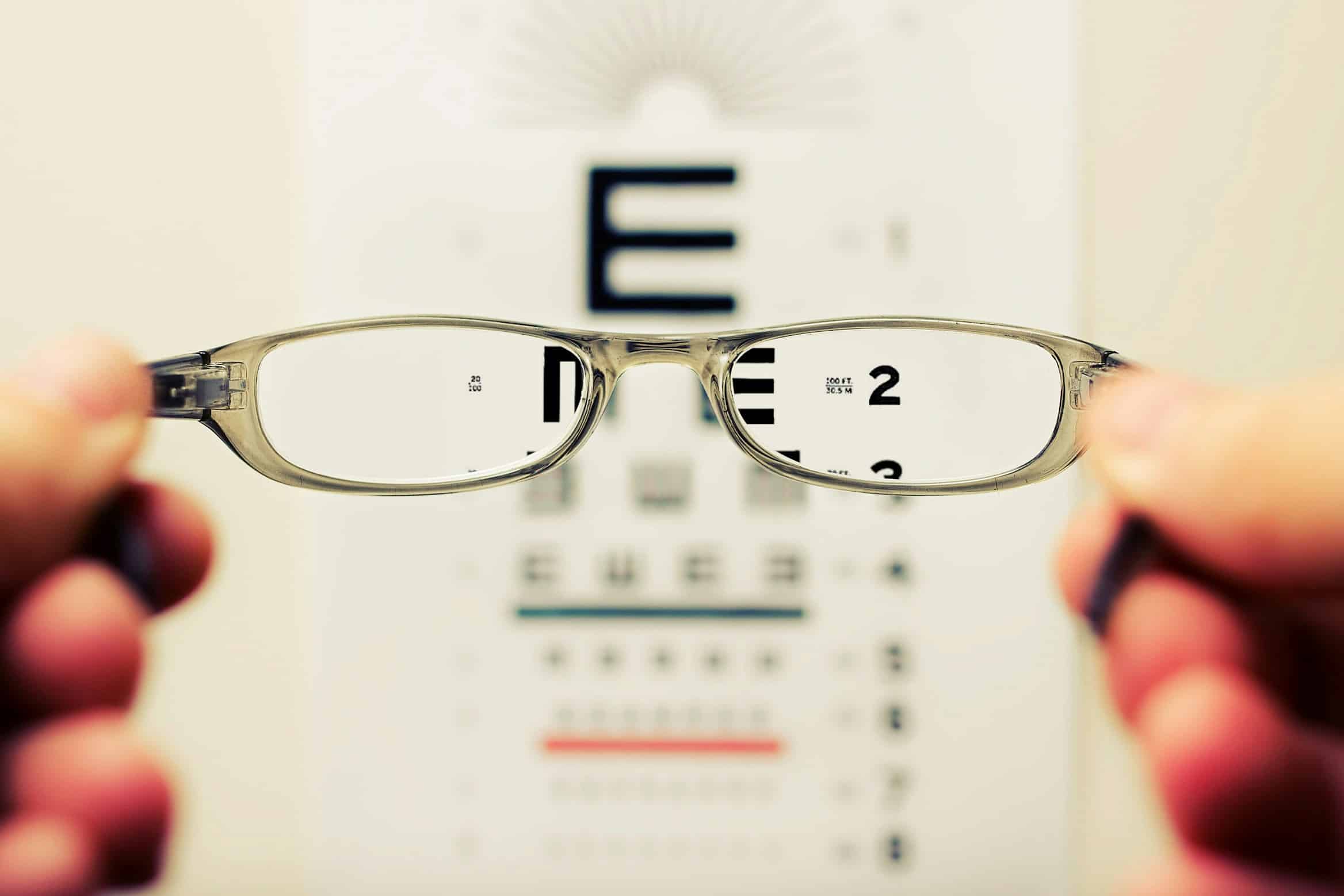 A person holds eyeglasses in front of an eye chart; the chart appears blurred except for the area seen through the lenses, highlighting the clarity that laser eye clinic content marketing can help communicate. Laser Eye Clinic Content Marketing And Website Redesign Success Story