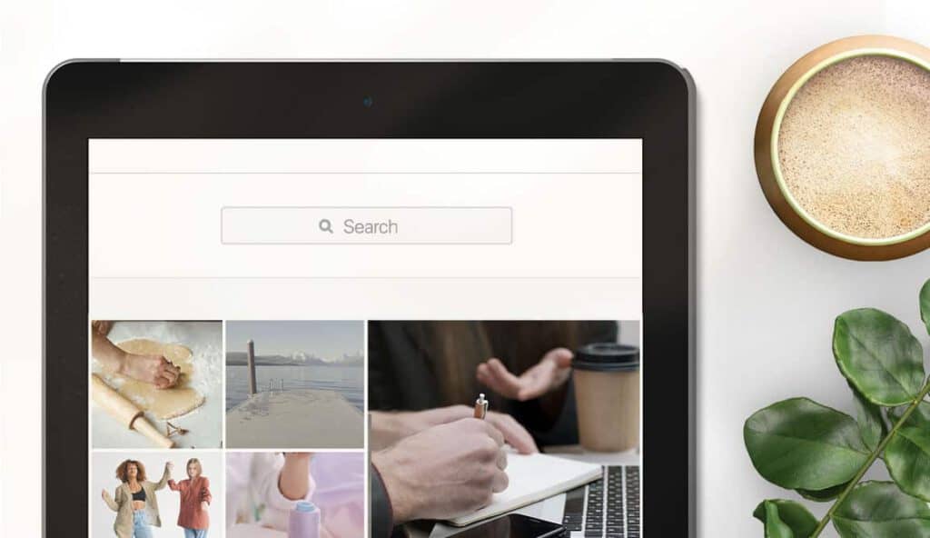 Flat lay of tablet zoomed into a search bar with Instagram grid-like images below. Coffee cup and plant at the side. Instagram search and explore