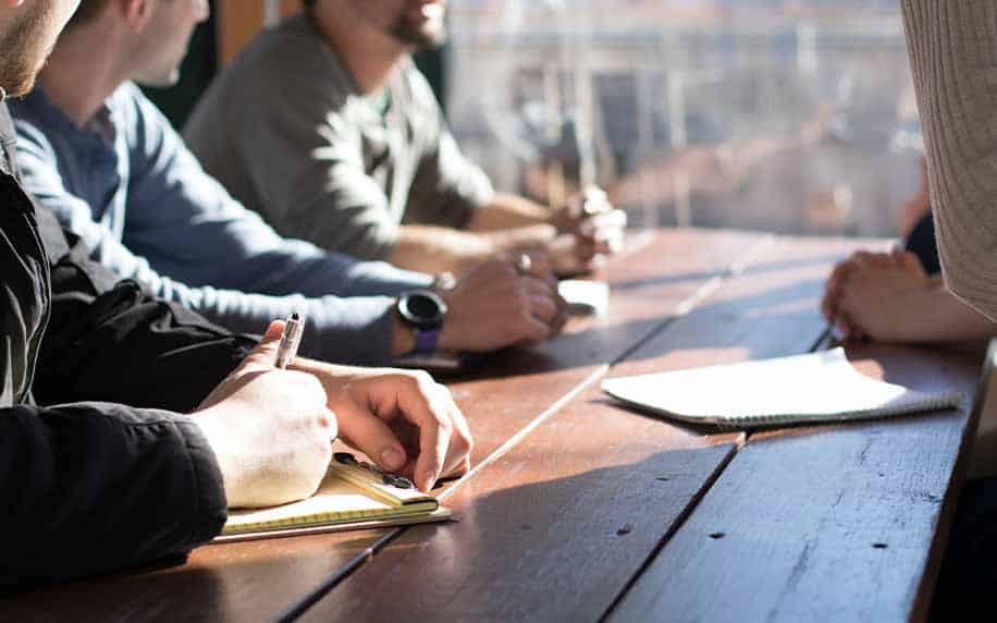 a group of people with pens and paper discussing return on investment with LinkedIn Advertising