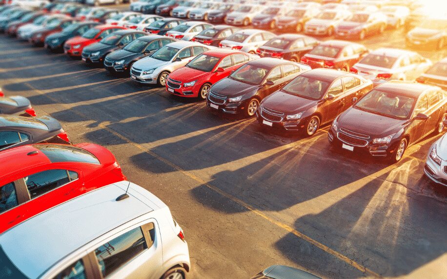 car dealership, row of cars outside in car park with sun shining in top right hand corner