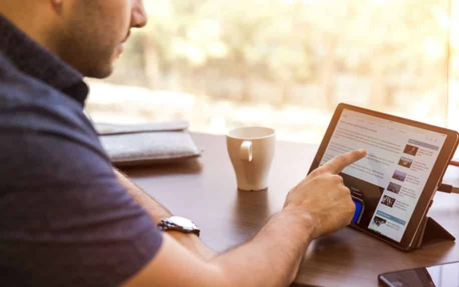 A photo of a man scrolling through LinkedIn on an iPad - create a company page on LinkedIn.