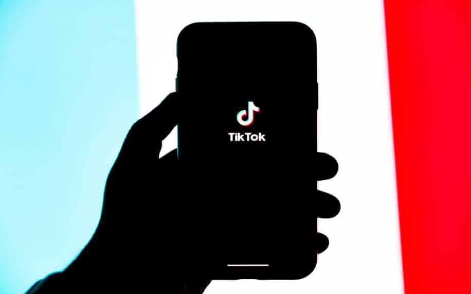 A man holding an iPhone with TikTok open, in front of a red, white, and blue background