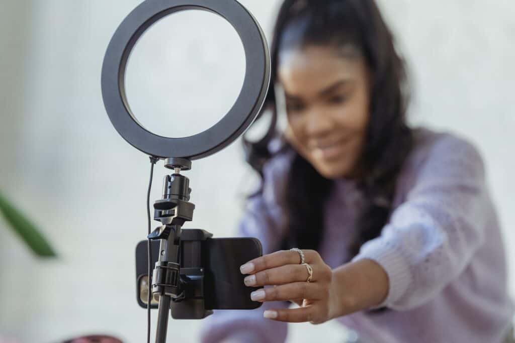 Happy young black woman setting up smartphone before shooting podcast