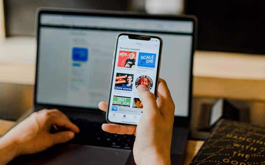 A man holding an iPhone showing a variety of podcasts available to listen to