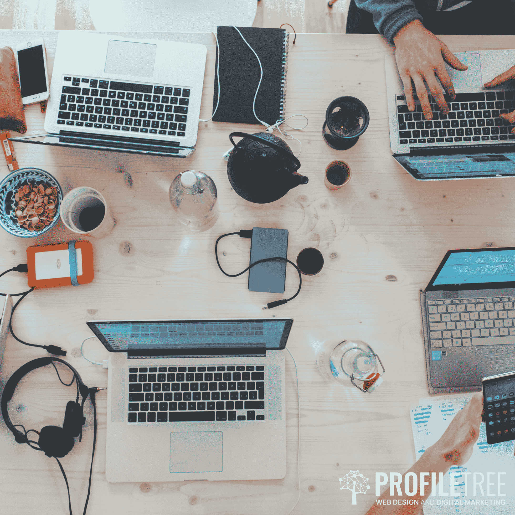 Image of several laptops together on a desk with people working on them