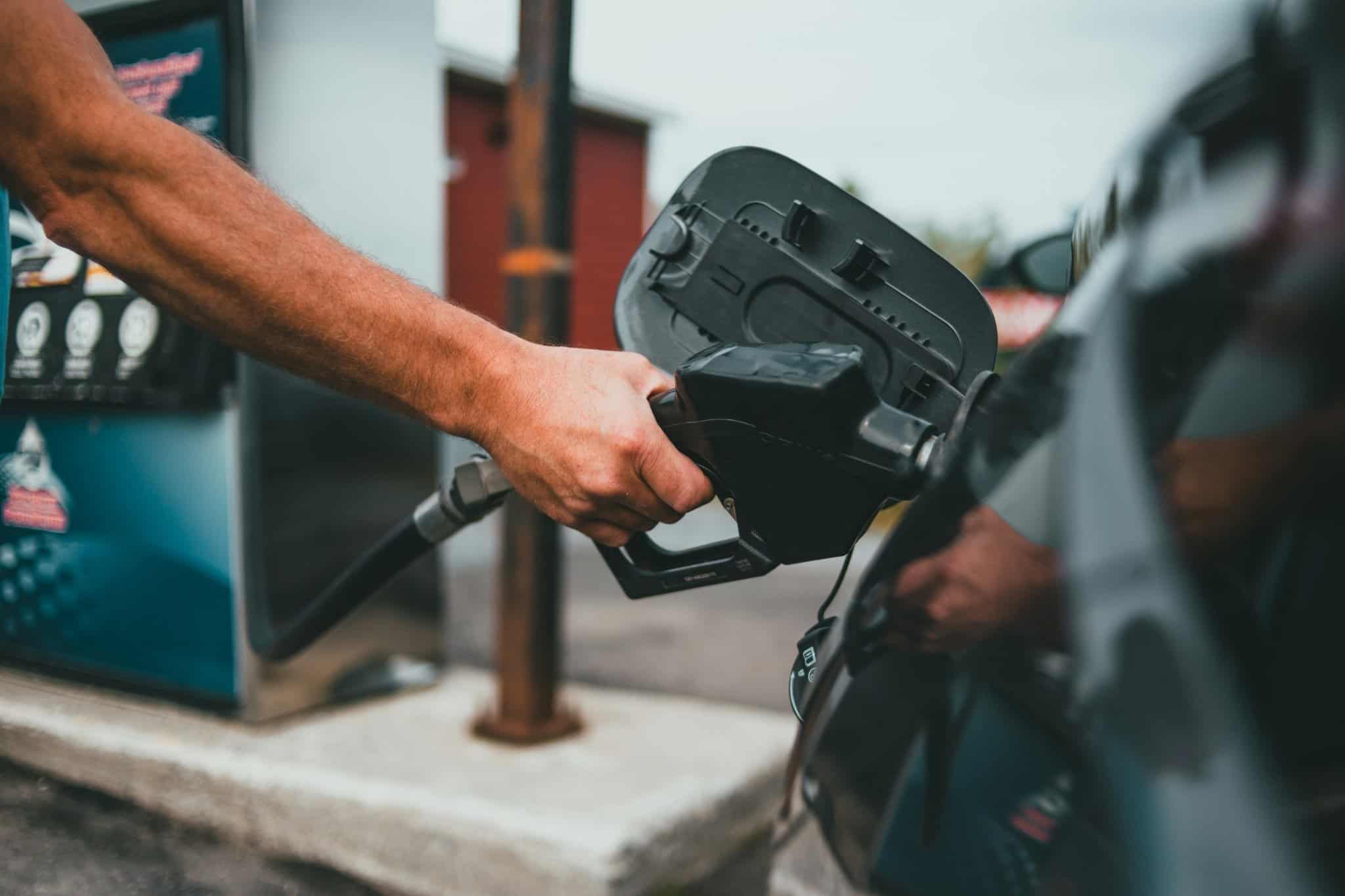 A person’s hand holds a fuel pump nozzle, filling a car with gas at a fuel station—an ideal scene for showcasing Website Design For A Petrol Station And Supermarket, with the focus on the hand and nozzle and a softly blurred background.