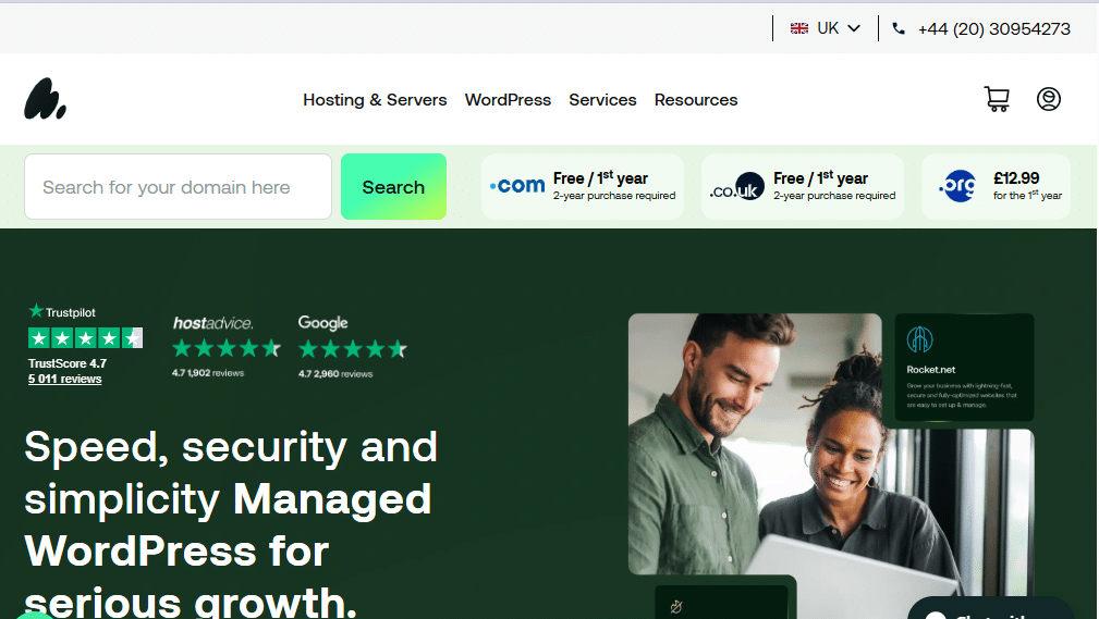 Screenshot of a web hosting company’s homepage featuring a search bar, domain pricing, contact number, review ratings, and two people looking at a laptop, with the headline highlighting A2 Hosting’s managed WordPress Hosting.