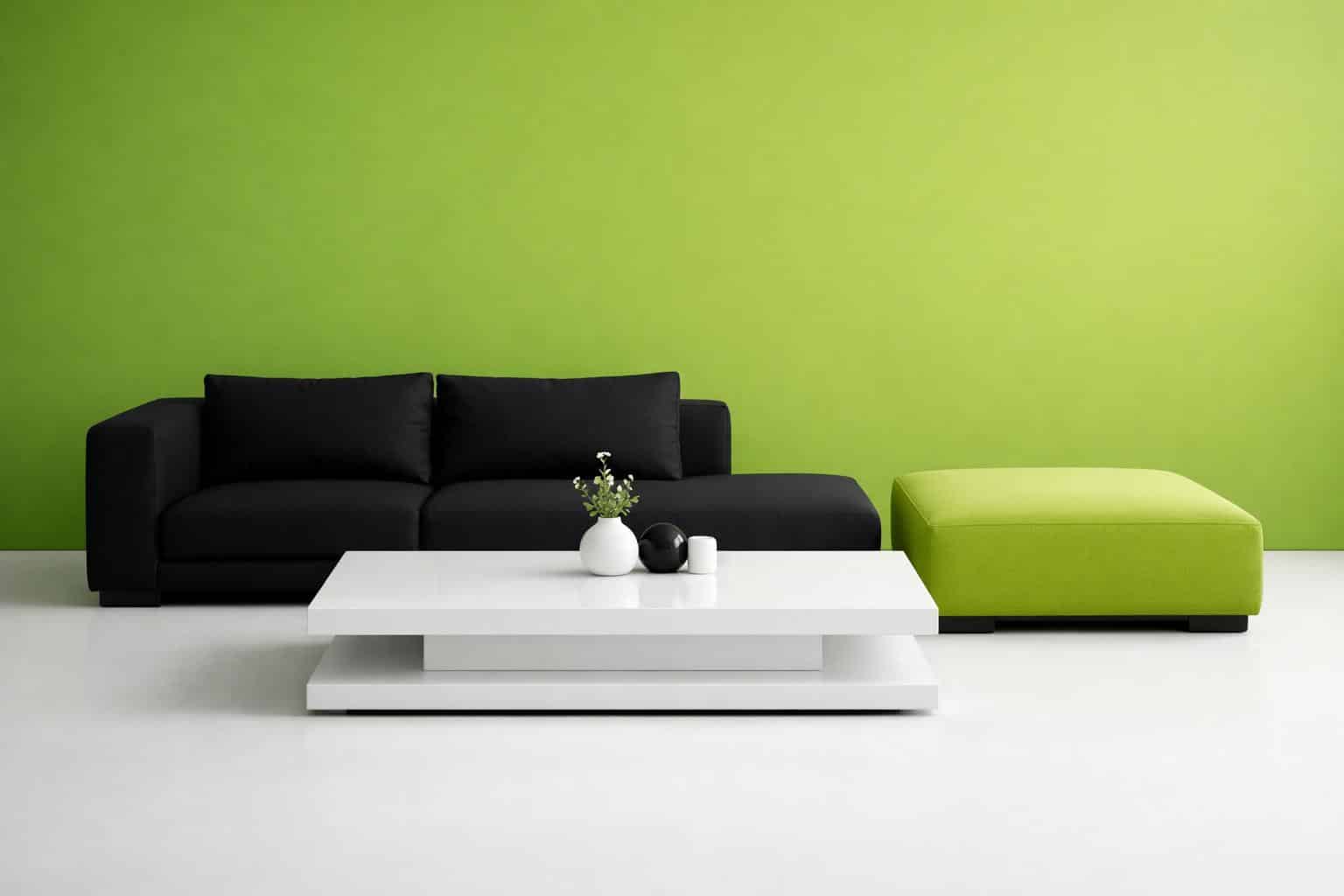 A modern living room with a black sofa, green ottoman, and white coffee table holding small decorative items is featured in this stylish furniture ecommerce website design, set against a bright green wall and white floor.